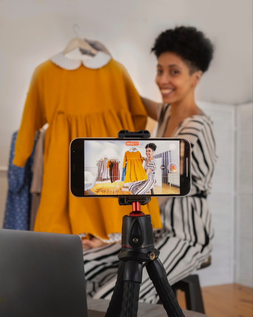 Smiling woman recording a video while showing a yellow dress.