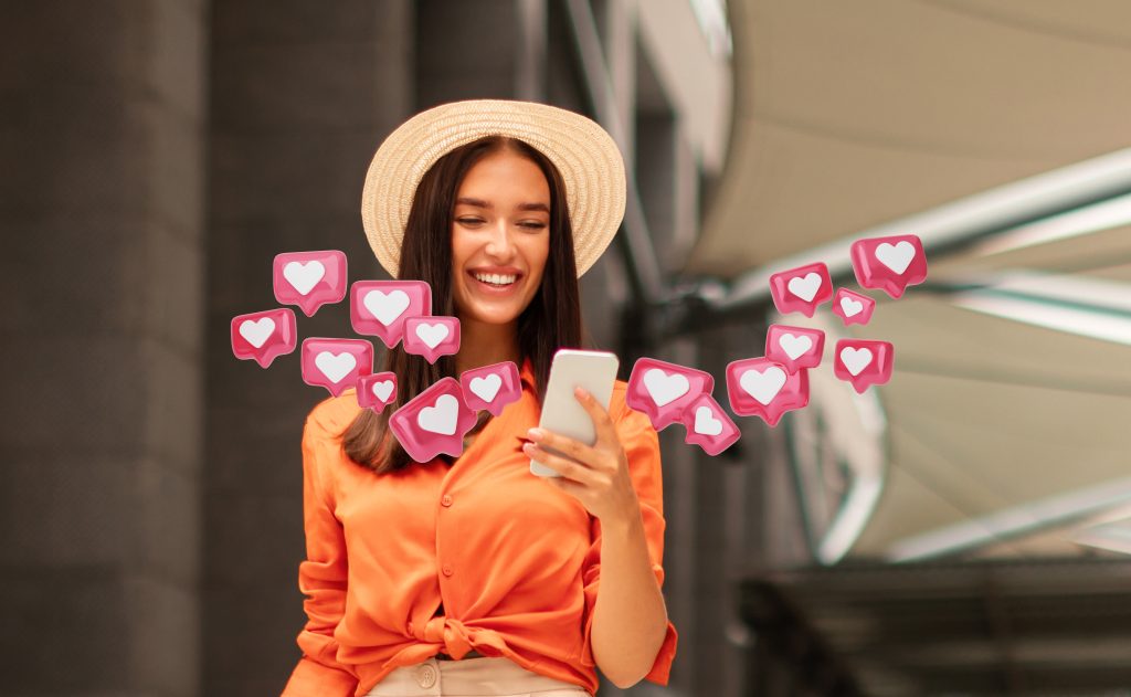 smiling woman using smartphone with social media hearts scaled